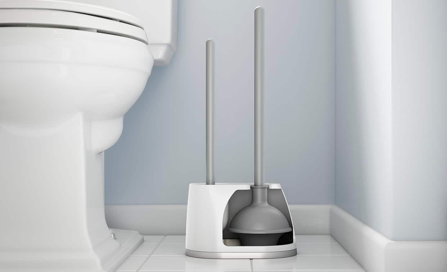 A plunger sits next to a toilet in a bathroom.