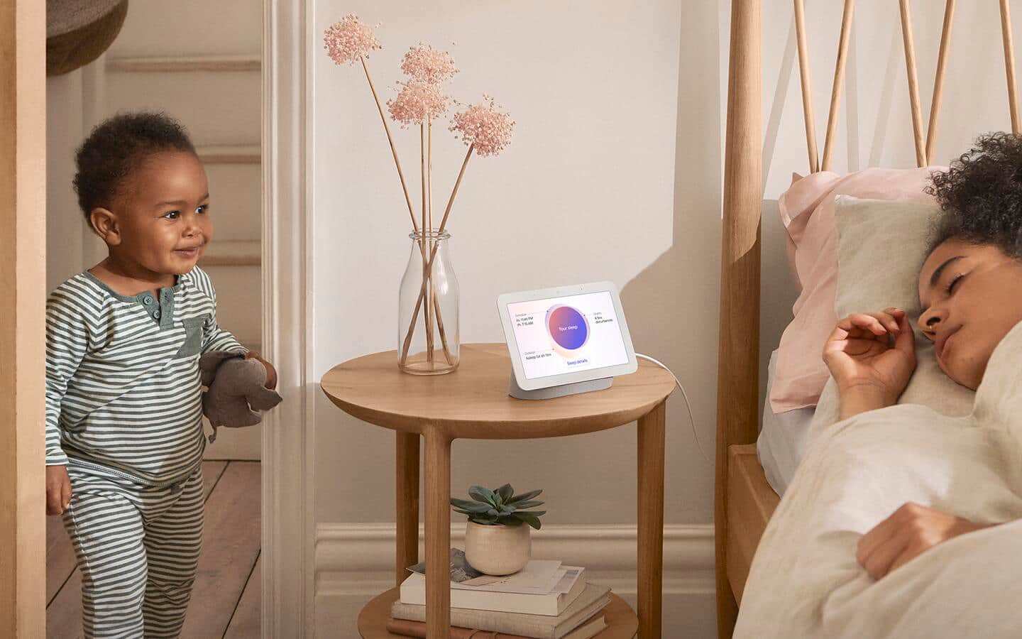 A small child entering a room with a smart display visible that indicates movement in the home while nearby, a woman sleeps in a bed.