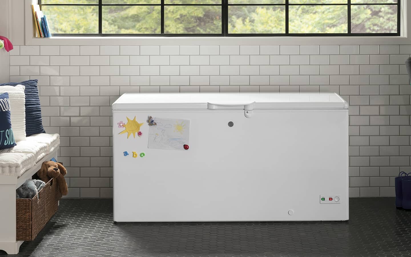 A white chest freezer sits under the window in a mudroom.