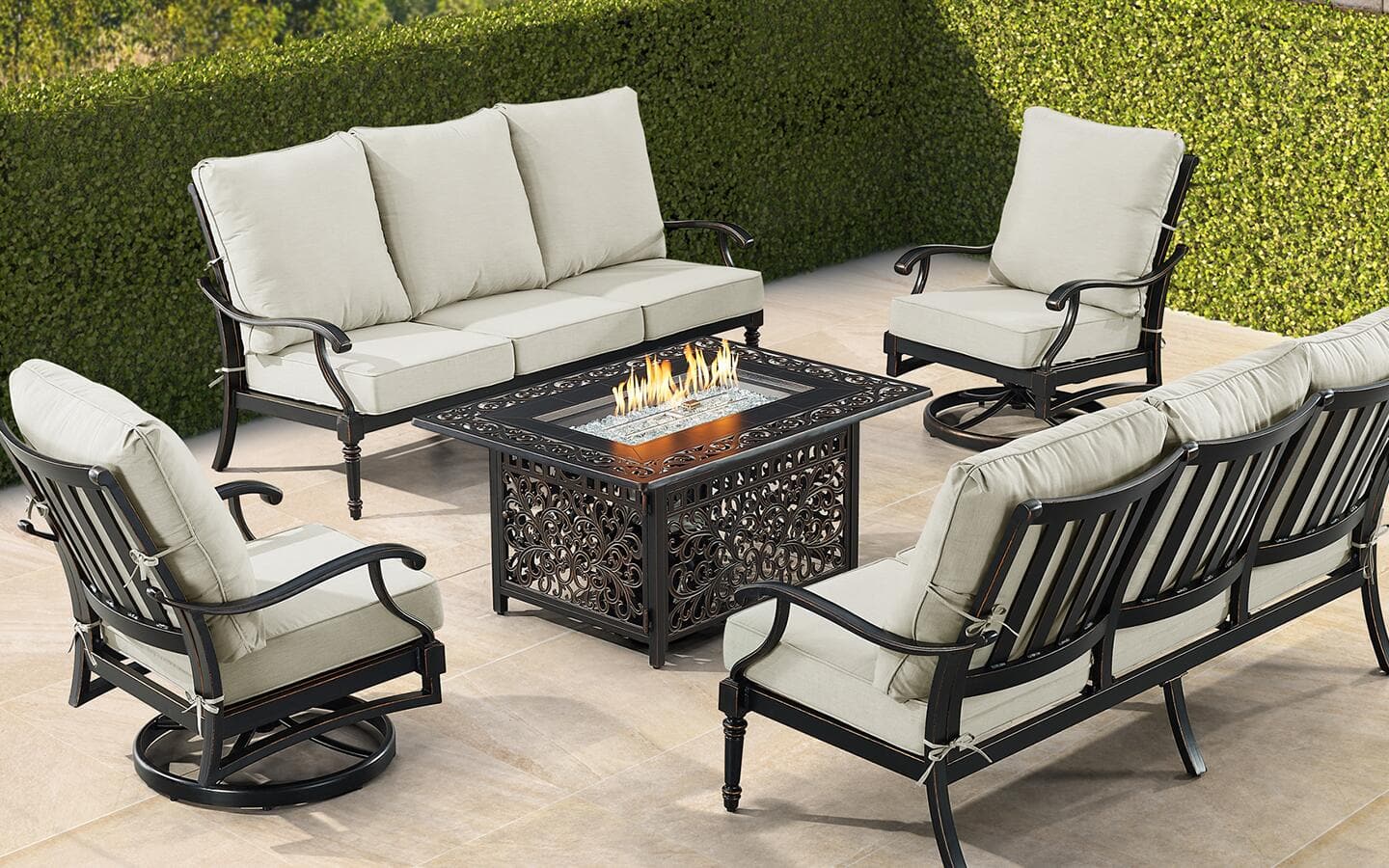 A fire pit table in the center of a patio conversation set with a loveseat and two chairs.