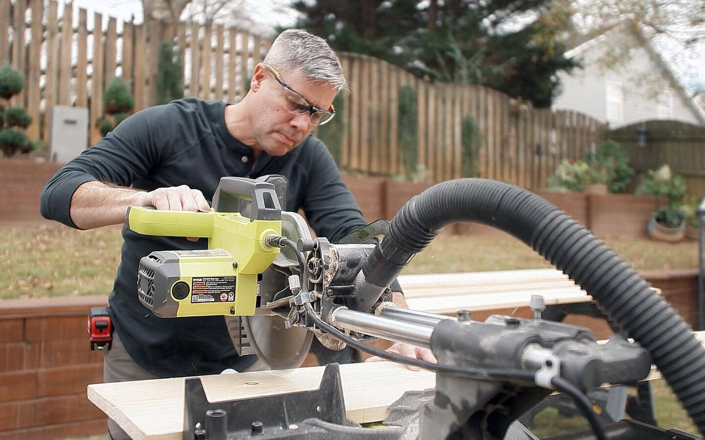 A man using a circular saw outdoors to cut boards for shelf supports.