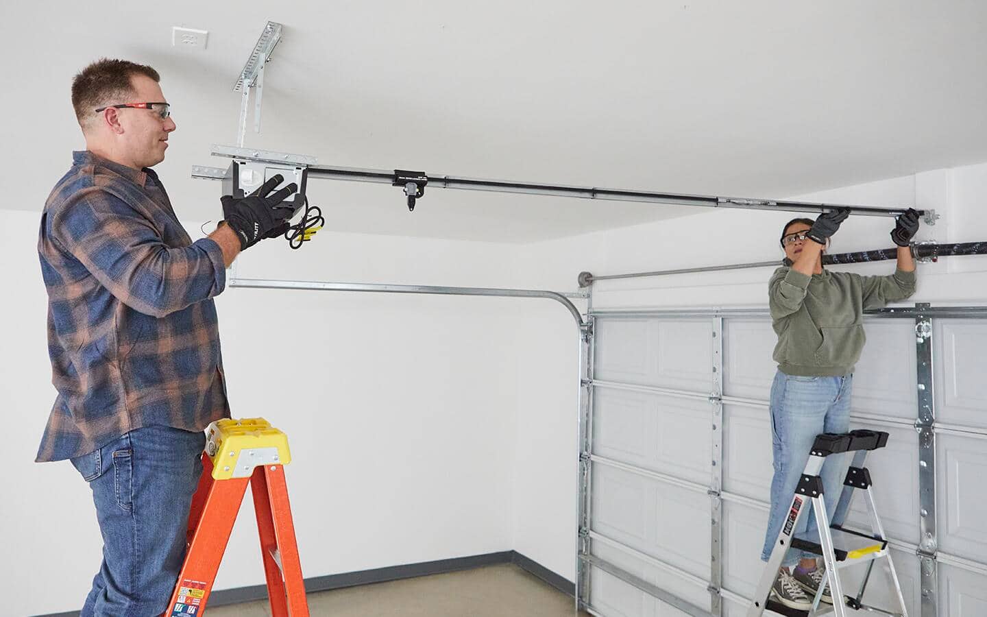 Two people suspend the smart garage door opener carriage tube from a garage ceiling