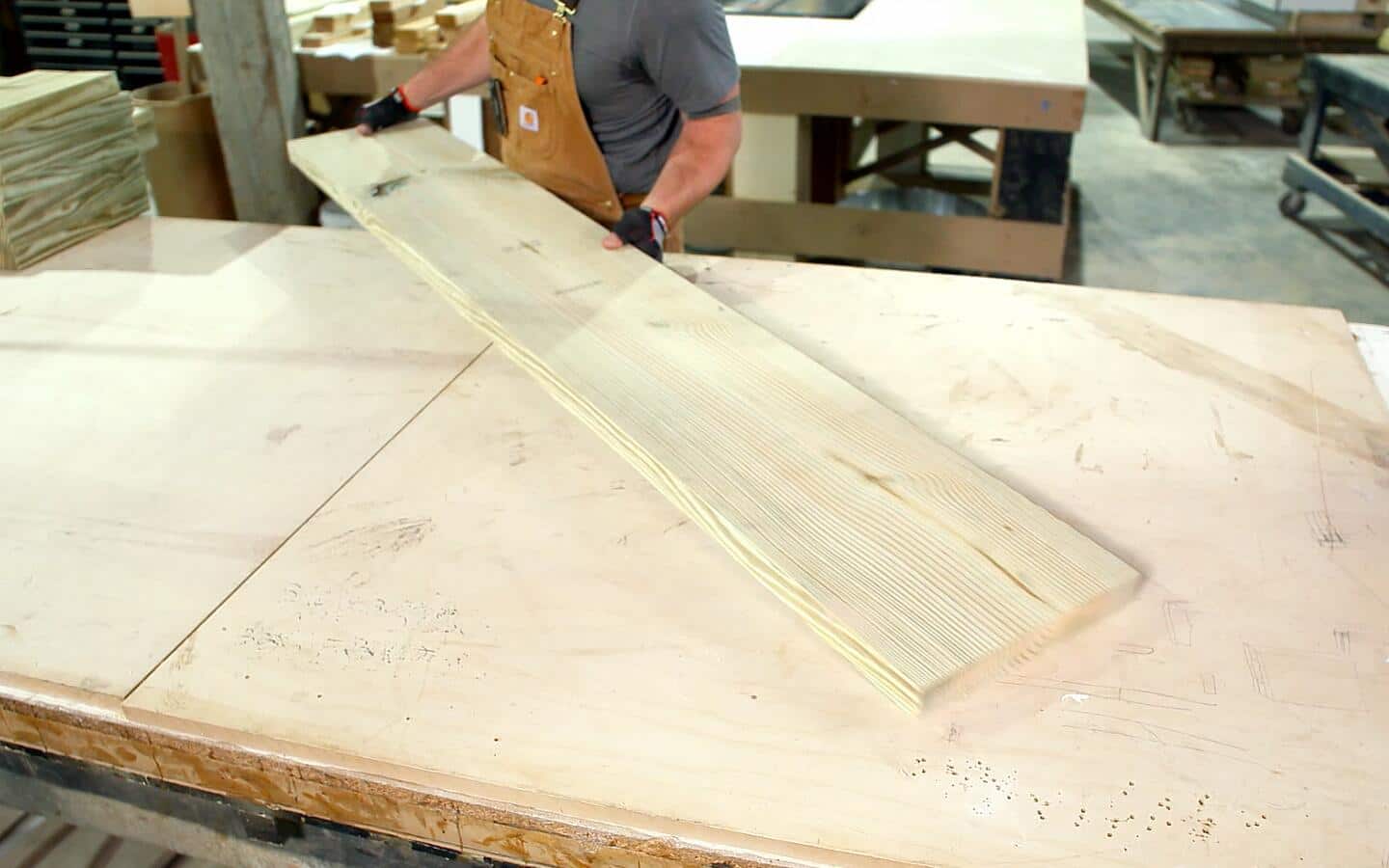 A person in a brown apron placing a large wooden board on a worktable.