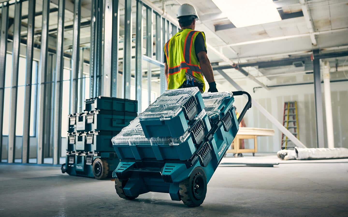A construction worker pulls a modular tool storage system through a commercial construction job site with unfinished drywall and steel studs..