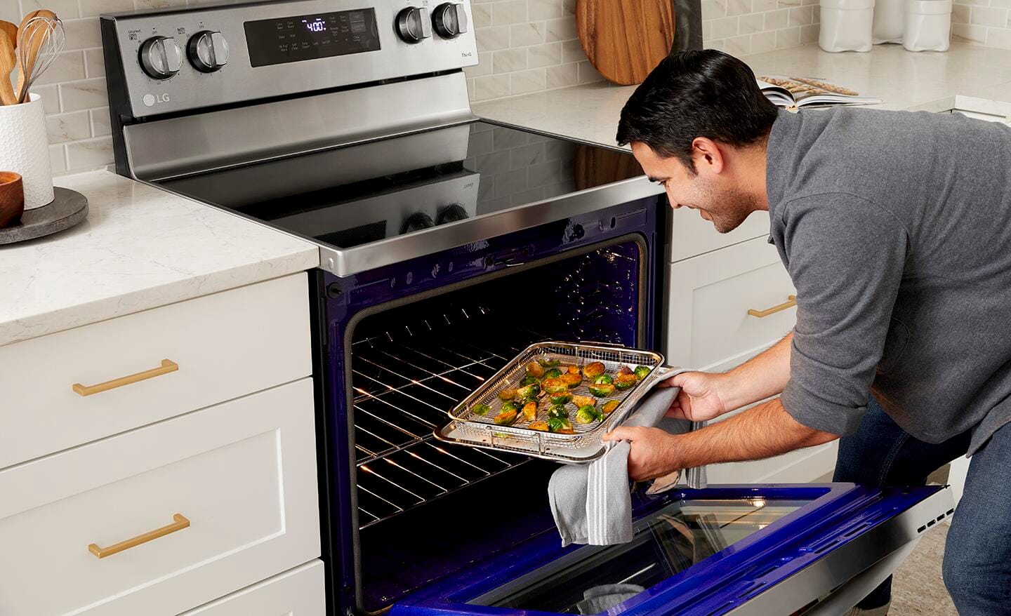 A person takes out a tray of food from a convection oven with an air fry capability.