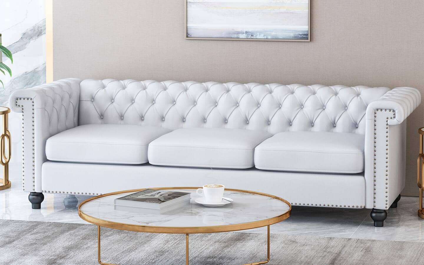 A circular glass and metal table placed in front of a white Tuxedo couch. A circular glass and metal table placed in front of a white Tuxedo couch.