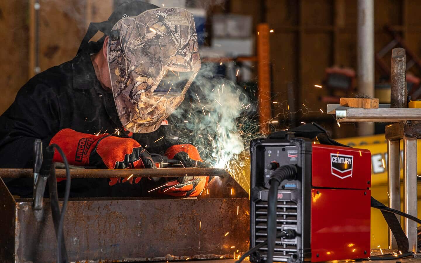 A person in protective gear welding metal, near a toolbox and electric welder engine.
