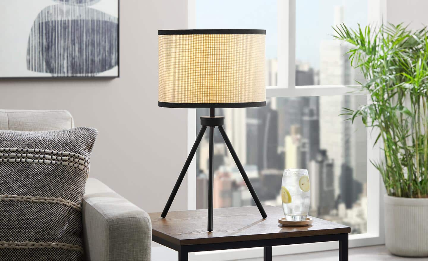 A tripod table lamp sits on an end table next to a grey sofa.