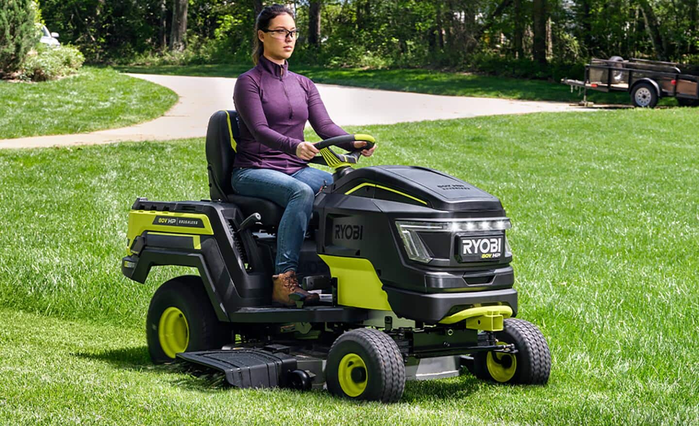 A woman mows grass with a battery powered riding lawn mower.