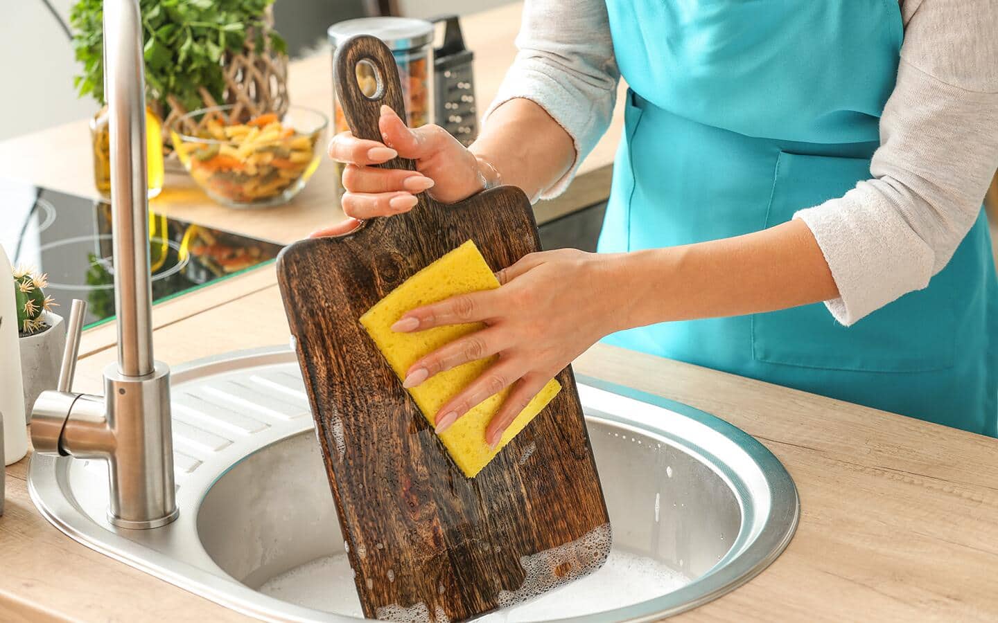 A woman washes a wooden cutting board with soapy water in a sink. A woman washes a wooden cutting board with soapy water in a sink.