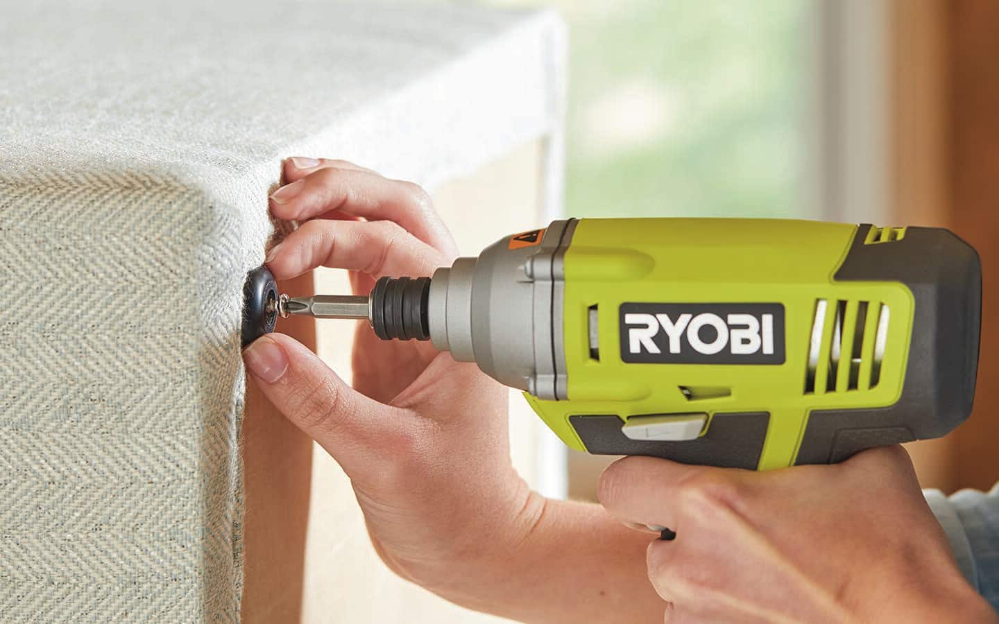 A person uses a power drill to fasten anti-skid pads to the ottoman. A person uses a power drill to fasten anti-skid pads to the ottoman.