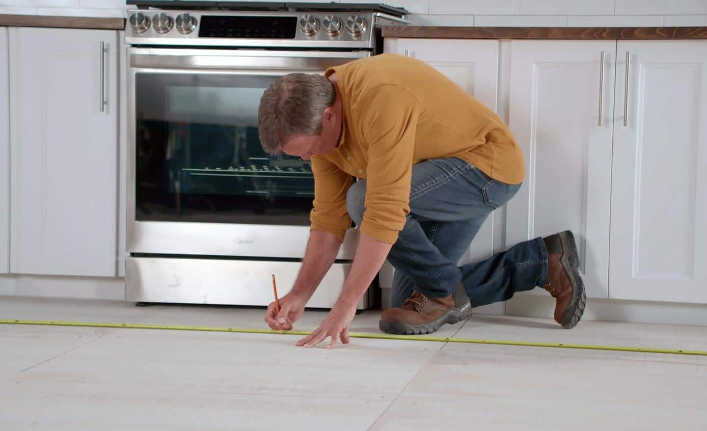 A man measures and marks gridlines for tile layout.