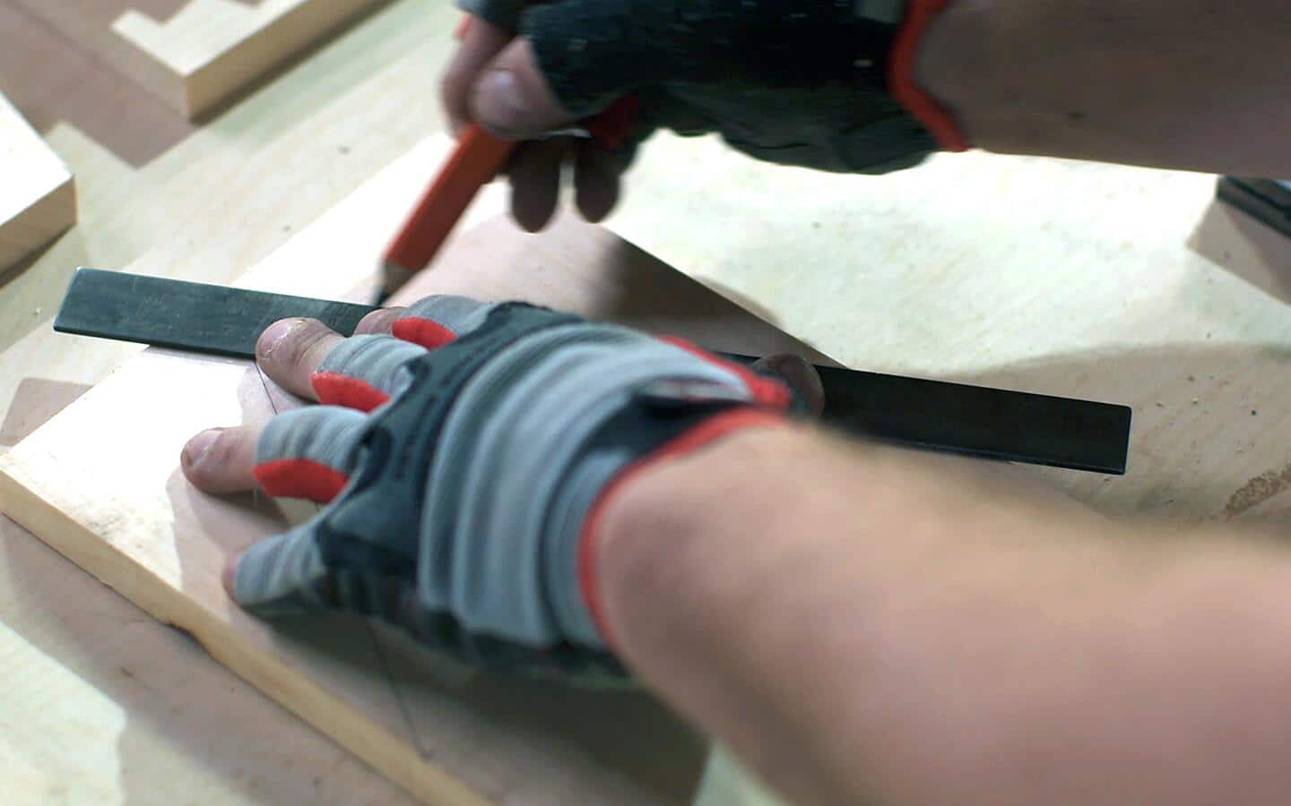 A gloved person marking the top of a wooden board to make cut lines for a birdhouse.