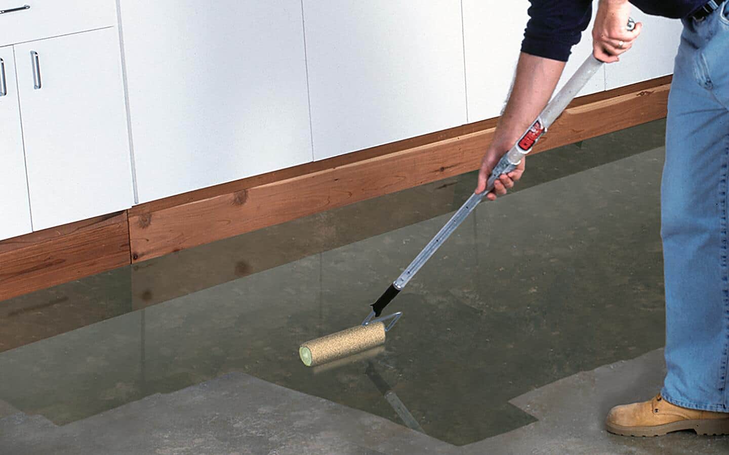 An individual using a roller to apply sealer to a concrete floor.