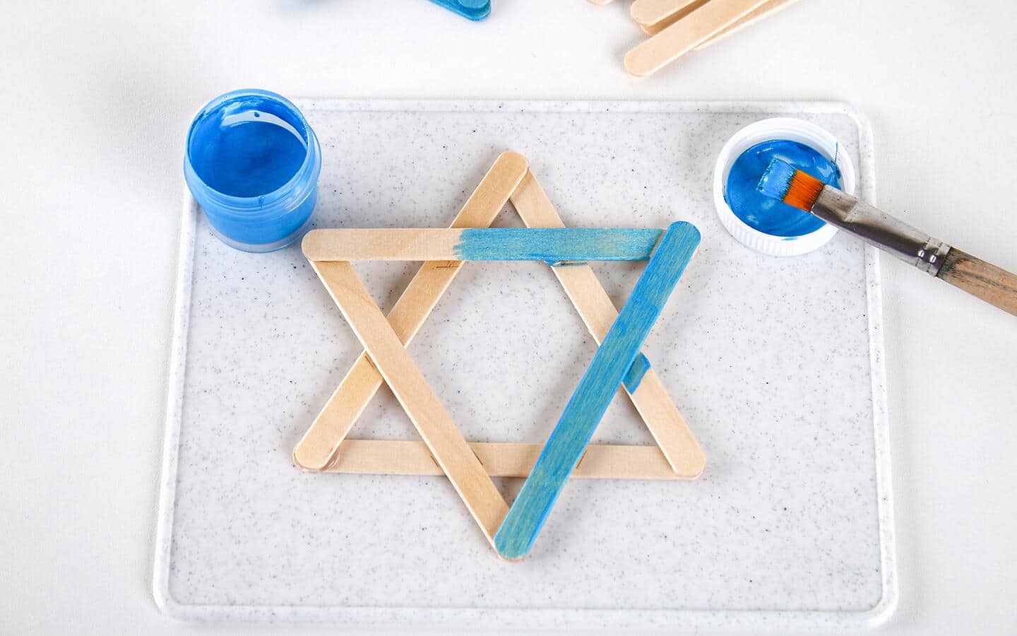 Someone painting a DIY Star of David made from popsicle sticks blue.