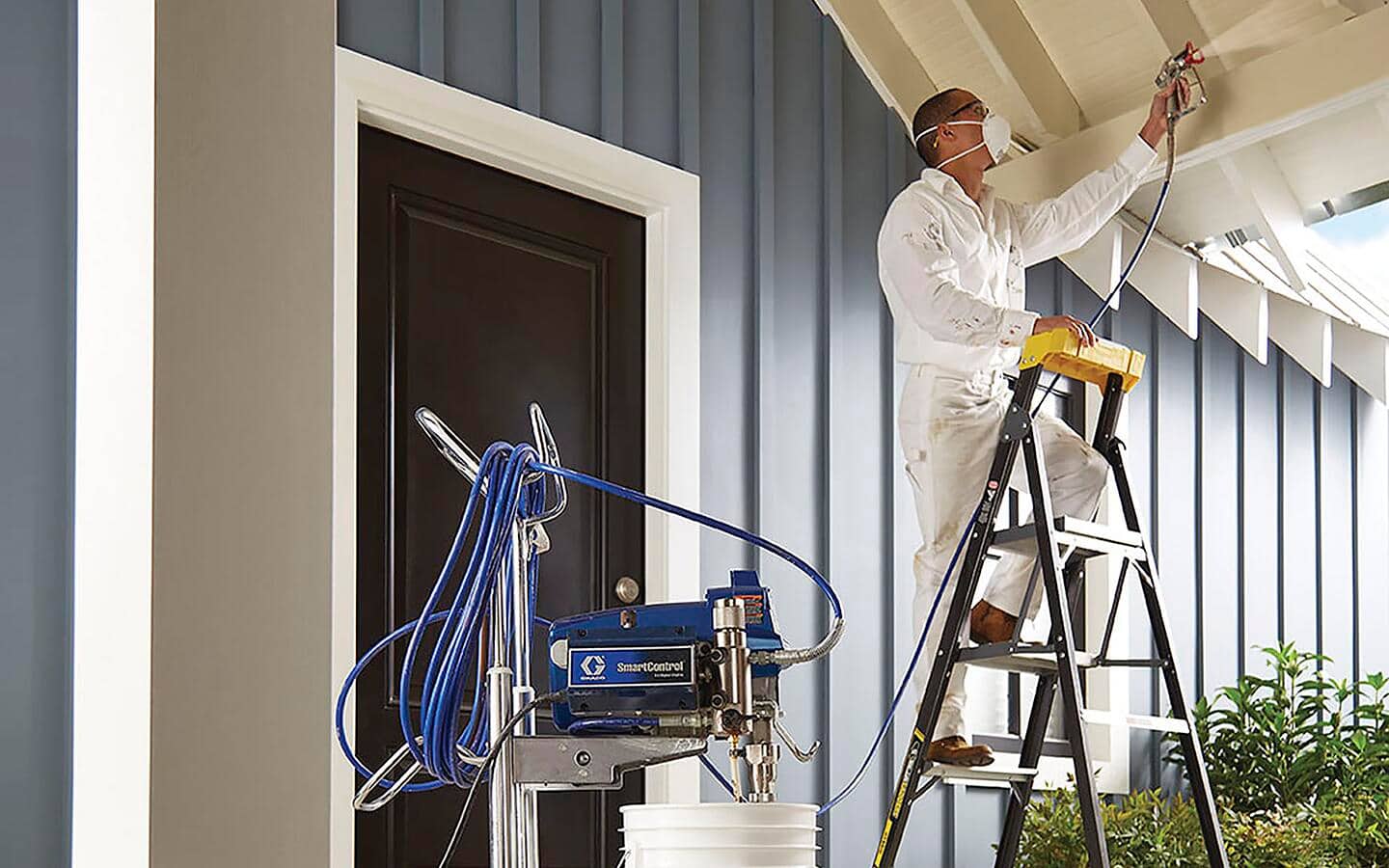 A man, standing on a step ladder, uses a professional paint sprayer to paint a porch ceiling. A man, standing on a step ladder, uses a professional paint sprayer to paint a porch ceiling.
