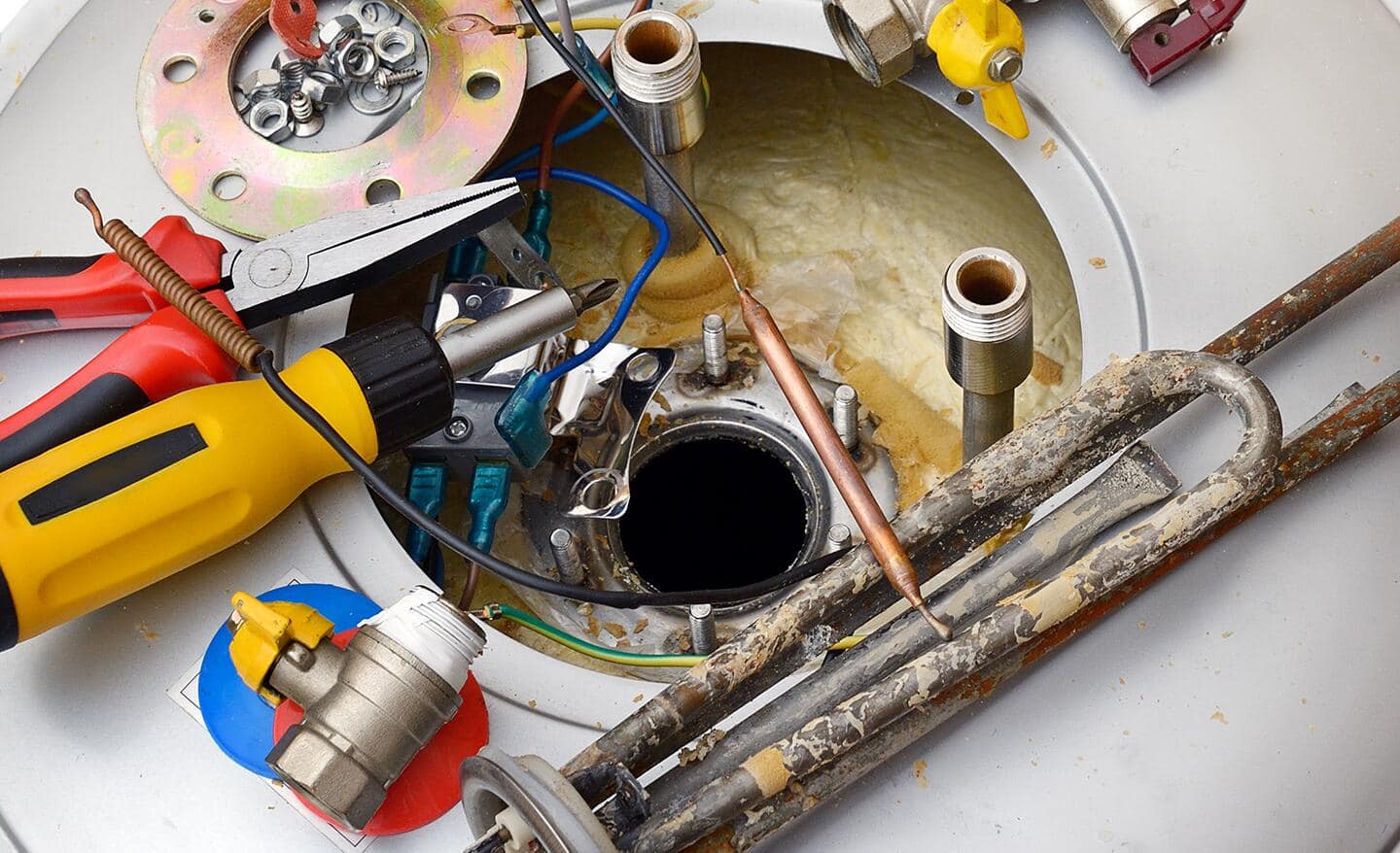 Tools and water heater parts on top of an open water heater. Tools and water heater parts on top of an open water heater.