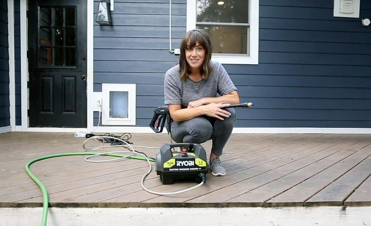 A woman with a pressure washer on a deck that is being prepared for refinishing.