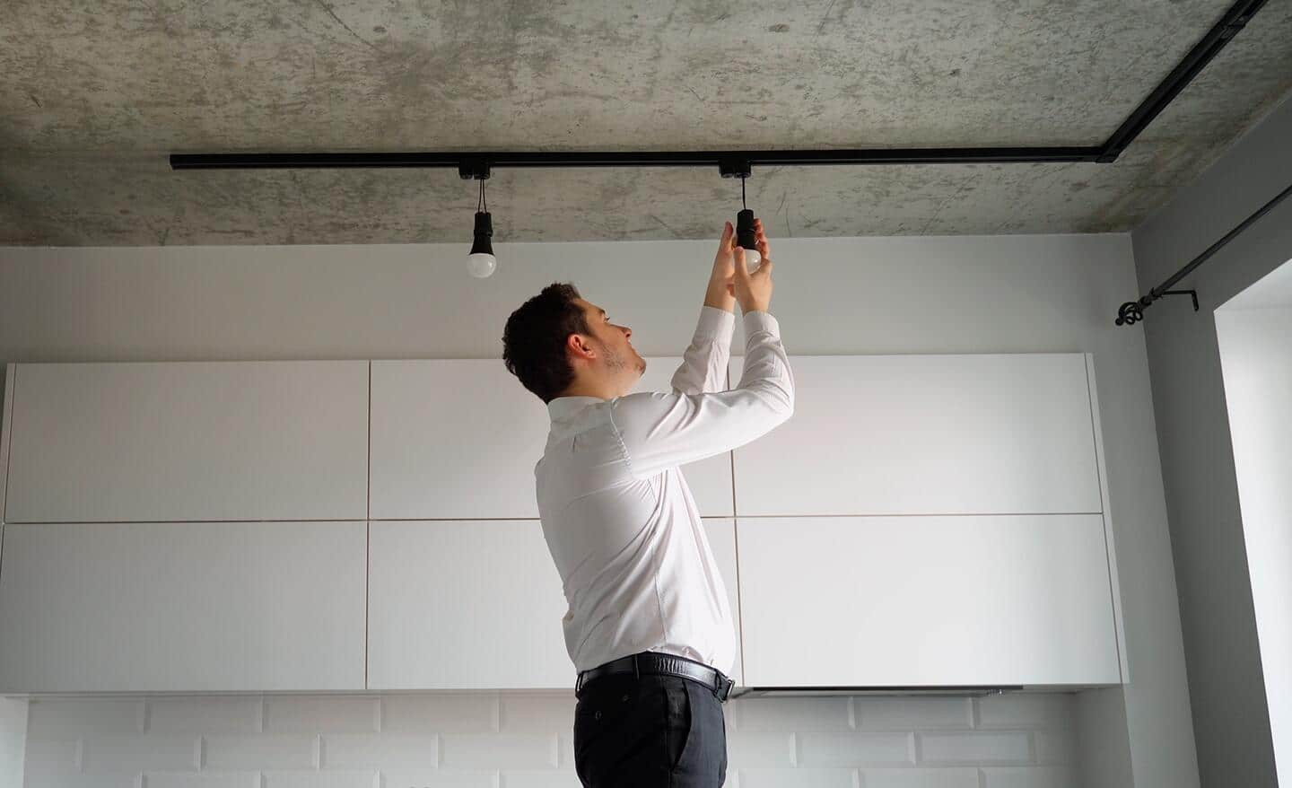 A person adjusts one of the fixtures of track lighting in front of a row of white cabinets.