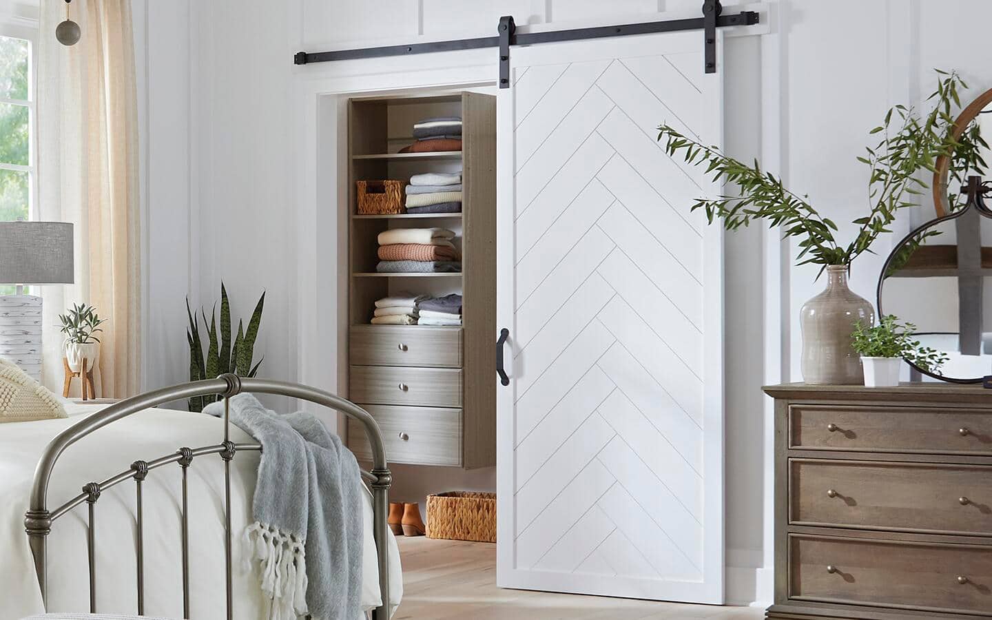 A white barn door opens in front of a closet in a bedroom with an iron bed. A white barn door opens in front of a closet in a bedroom with an iron bed.