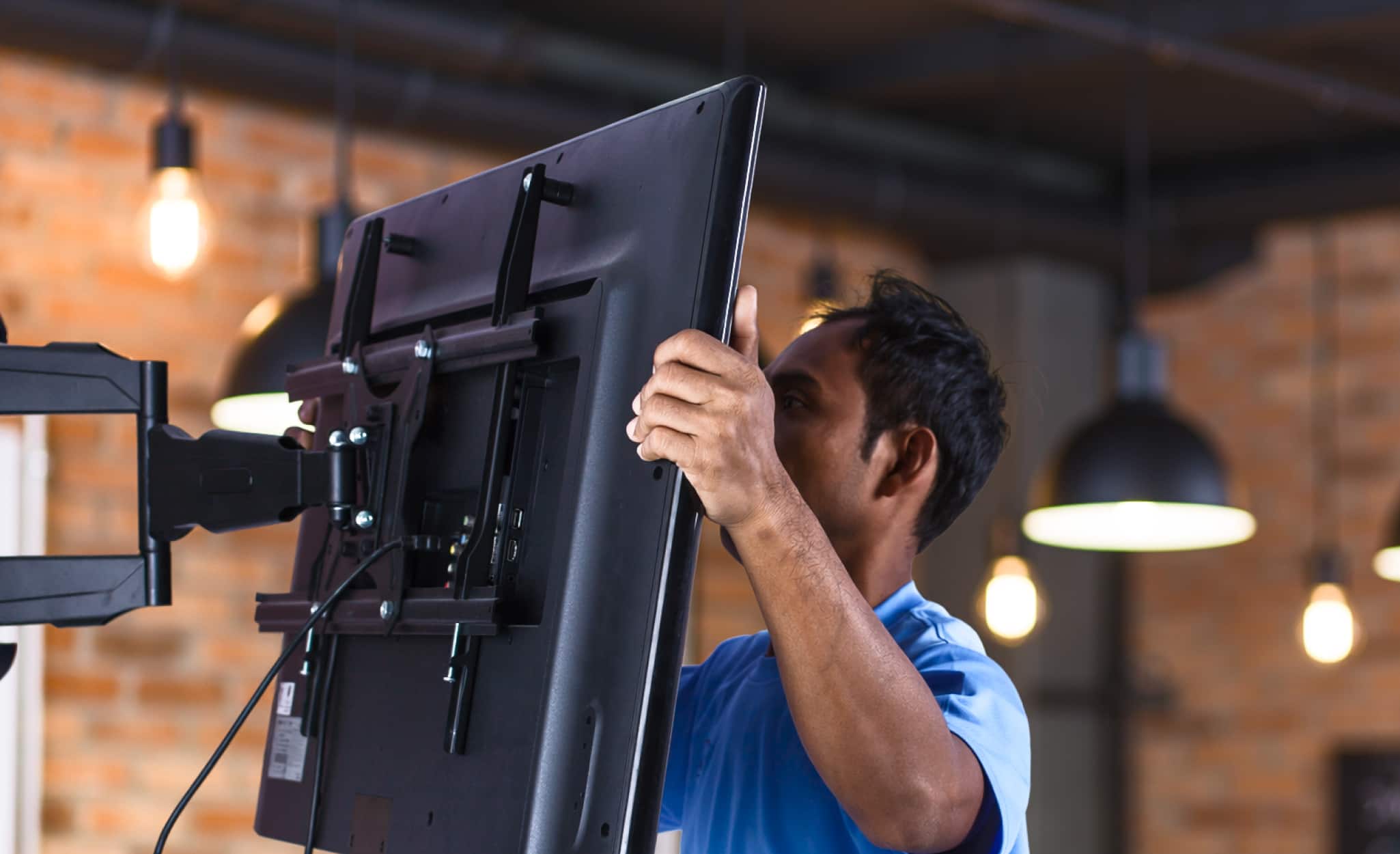 A Pro attaches a widescreen 4K TV to a wall mounting bracket.