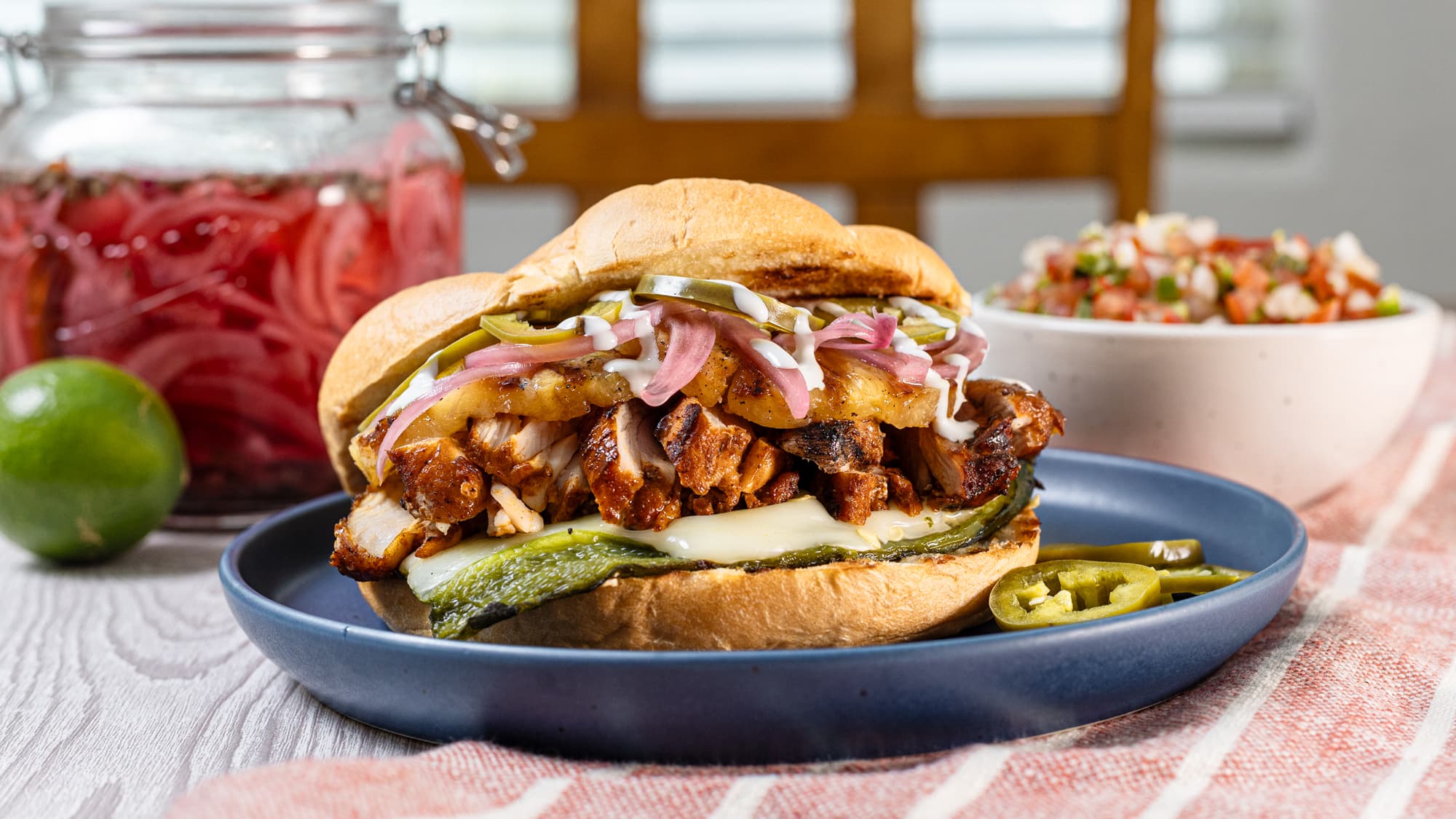 Plated grilled chicken torta over cheese stuffed poblano pepper on a bun, stuffed with pickled red onions, jalapeno, and crema. Plated grilled chicken torta over cheese stuffed poblano pepper on a bun, stuffed with pickled red onions, jalapeno, and crema.