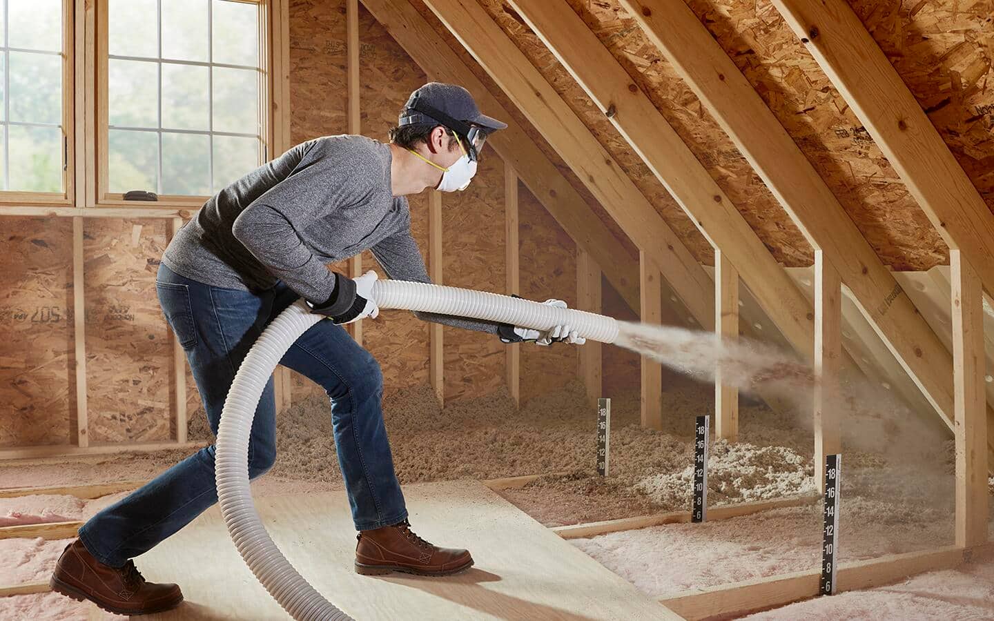 A man sprays loose insulation in an attic. A man sprays loose insulation in an attic.