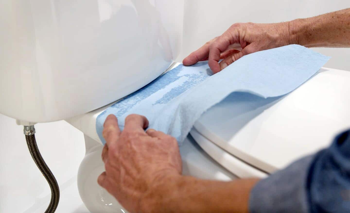 A man using a paper towel to find a water leak on a toilet.