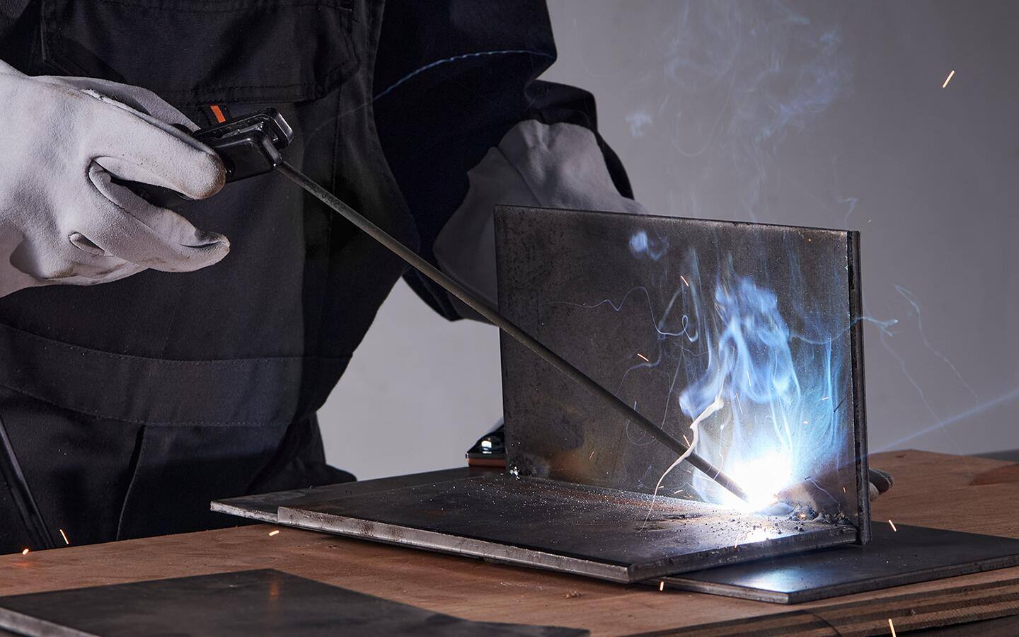 A gloved individual welding two metal sheets together.