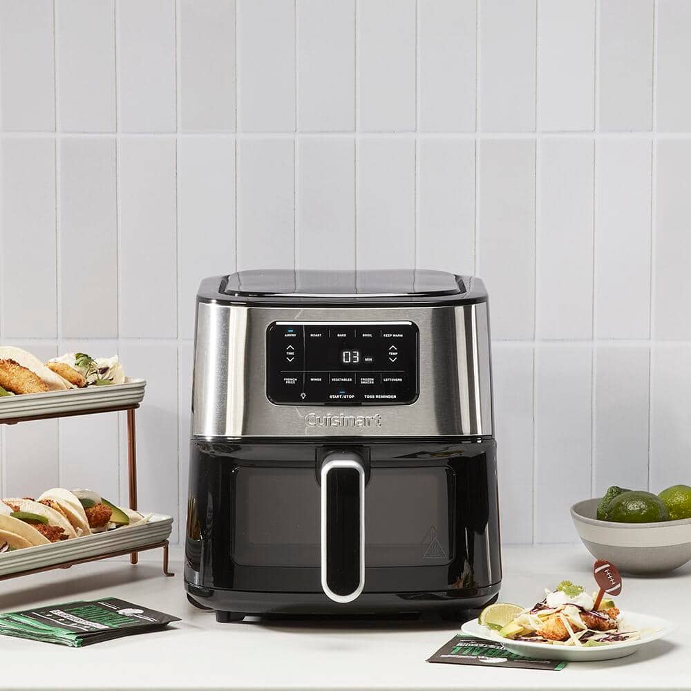 A stainless steel and black air fryer sits on a counter next to food selections.