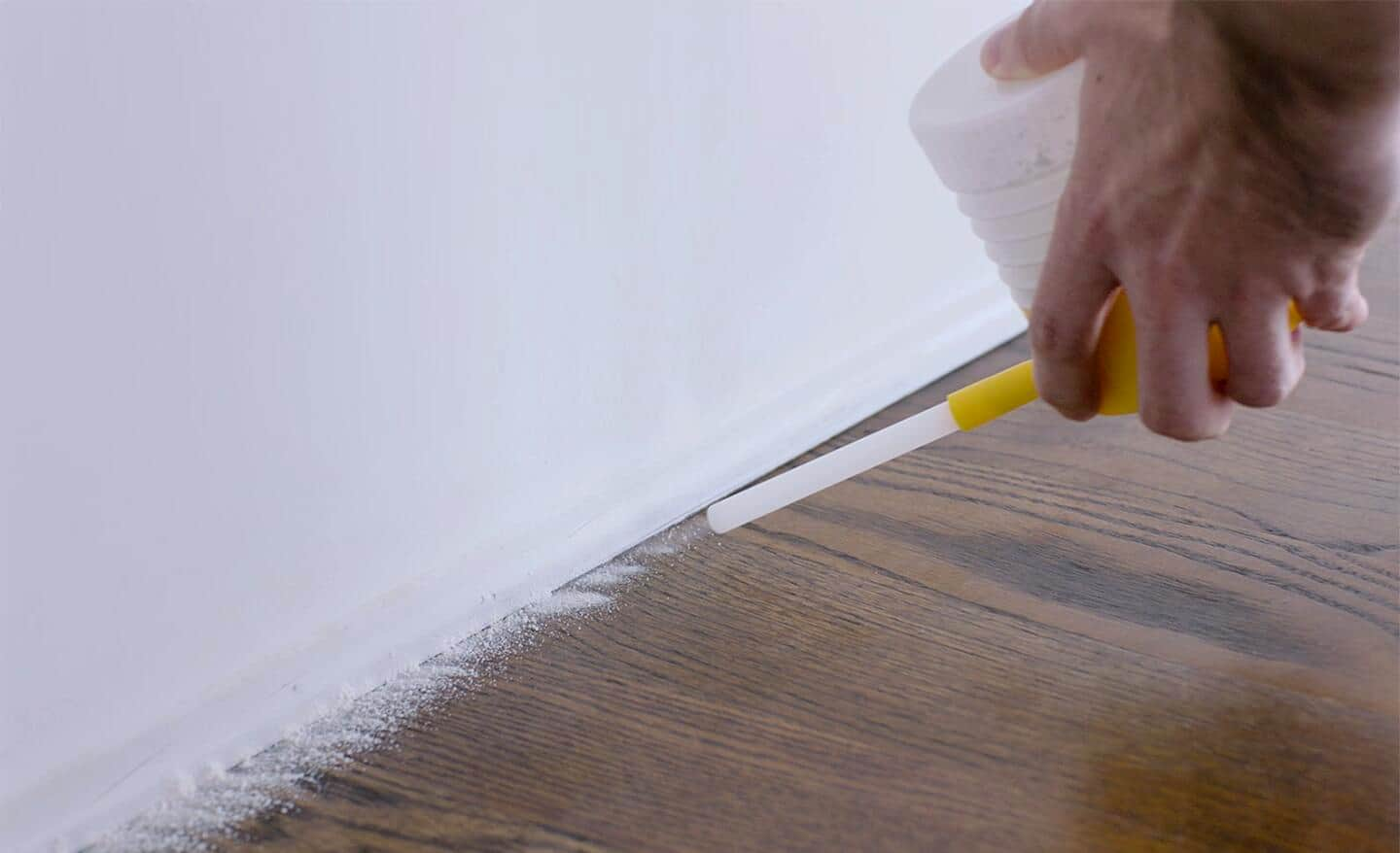 A person applying a cricket treatment along the baseboards of a home.