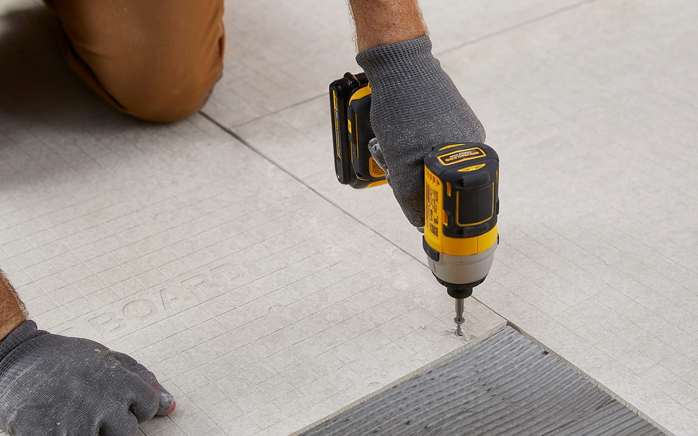 A Pro screwing in backer board into a subfloor.